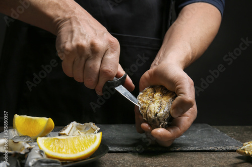 Man opening shell of fresh oyster on dark background