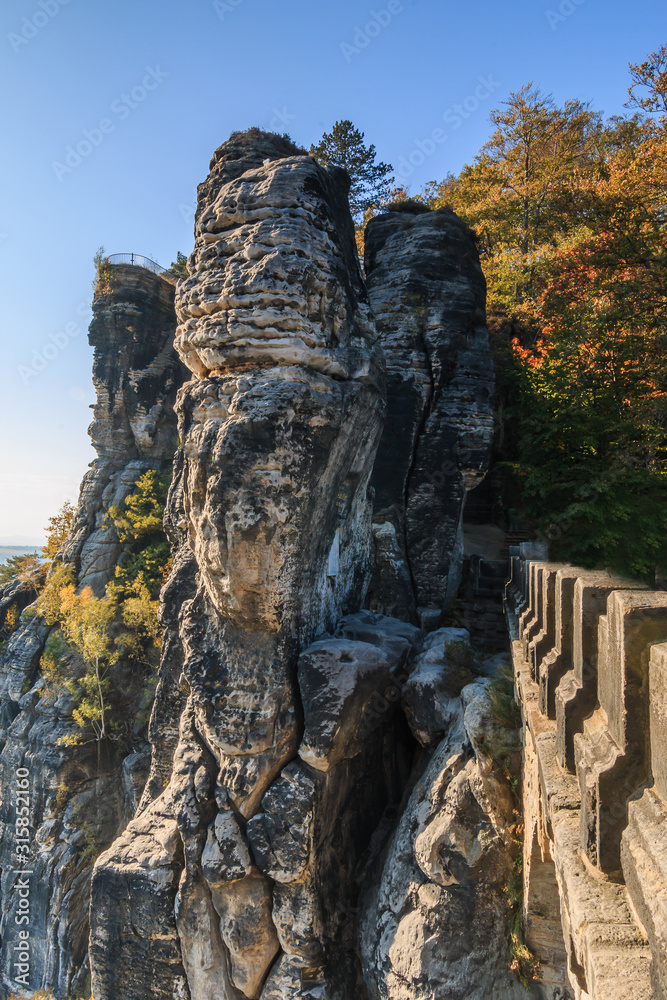 Lateral view of the Bastei bridge in Saxon Switzerland. Rocks and trees in autumn mood with a terrace view of the Elbe Sandstone Mountains with blue sky and sunshine