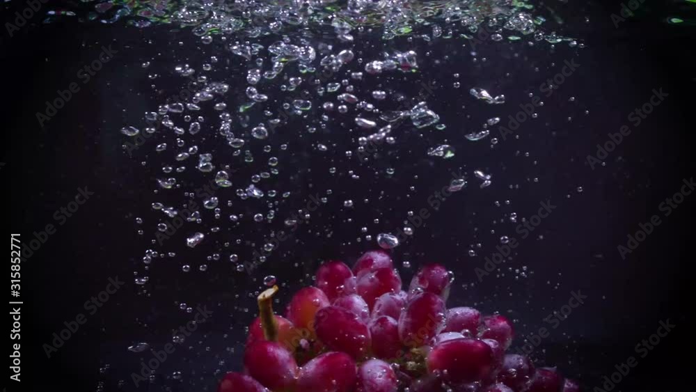 Red grapes fall into water with splashes super slow motion shot