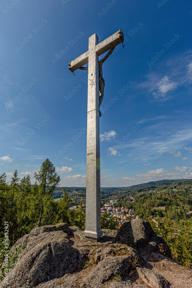 Nejdek / Czech Republic - September 15 2019: A crucifix with Jesus Christ statue standing on a hill called Kreuzberg overlooking Nejdek town. Sunny day with blue sky and white clouds. Vertical image.
