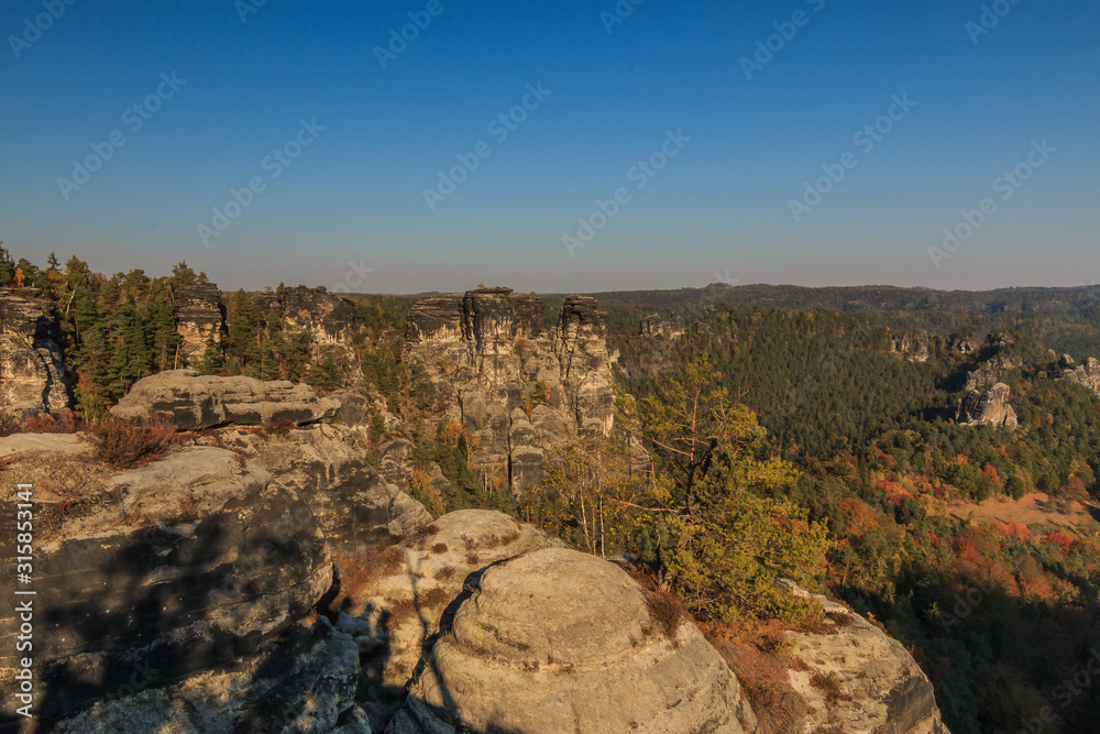Elbe Sandstone Mountains in autumn with sunshine and blue sky. Rock formation in Saxon Switzerland with deciduous and coniferous trees and forest in the background