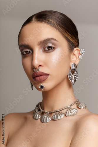 Magnificient look of a female model, with silver jewelery, looking with attitude at camera, over grey background.