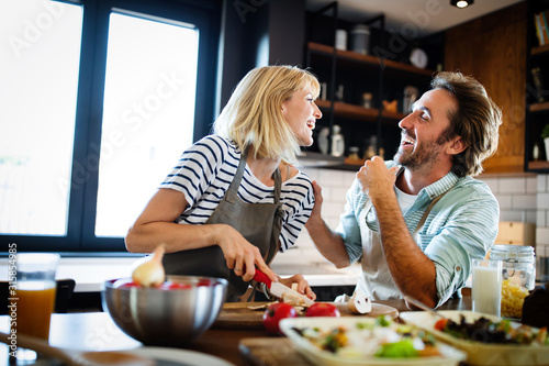 Obraz na plátne Beautiful young couple is talking and smiling while cooking healthy food in kitc