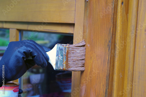 worker hand in glove with brush daubed a protective coating for wood on the window photo