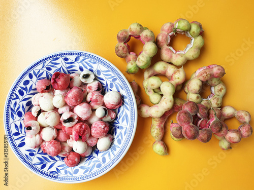 Peeled Manila Tamarind or makham thet in Thailand onto a beautiful patterned dish with many green and red Manila Tamarind decoration on yellow background photo