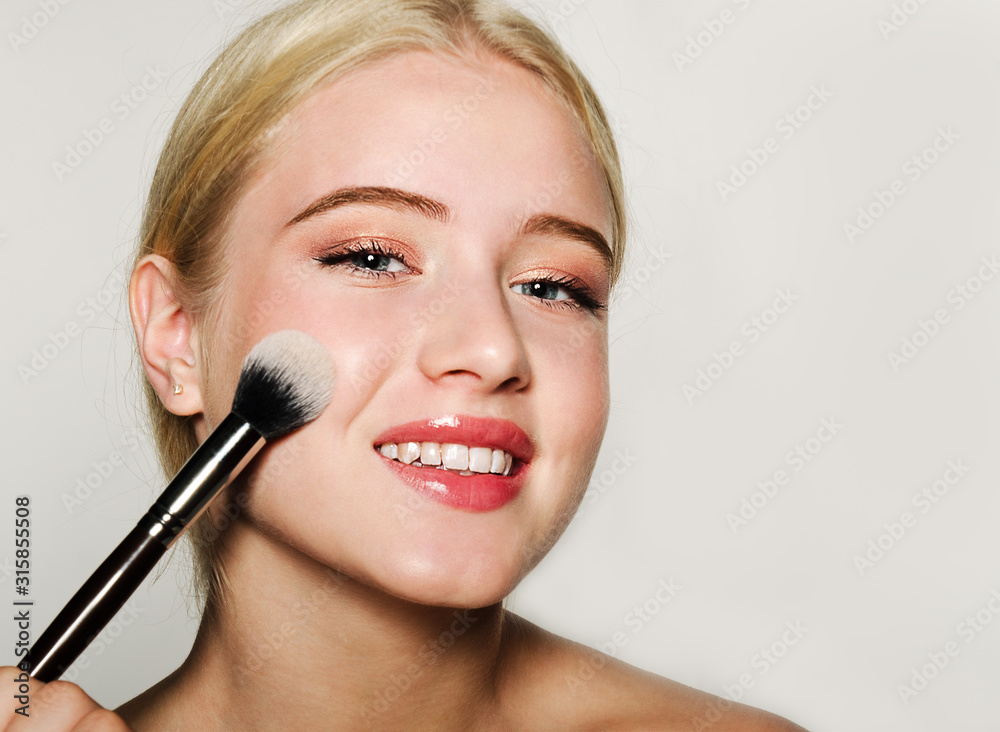 Portrait of beautiful blonde young woman face holding make up brushes. Spa model girl with fresh clean skin isolated on a white background