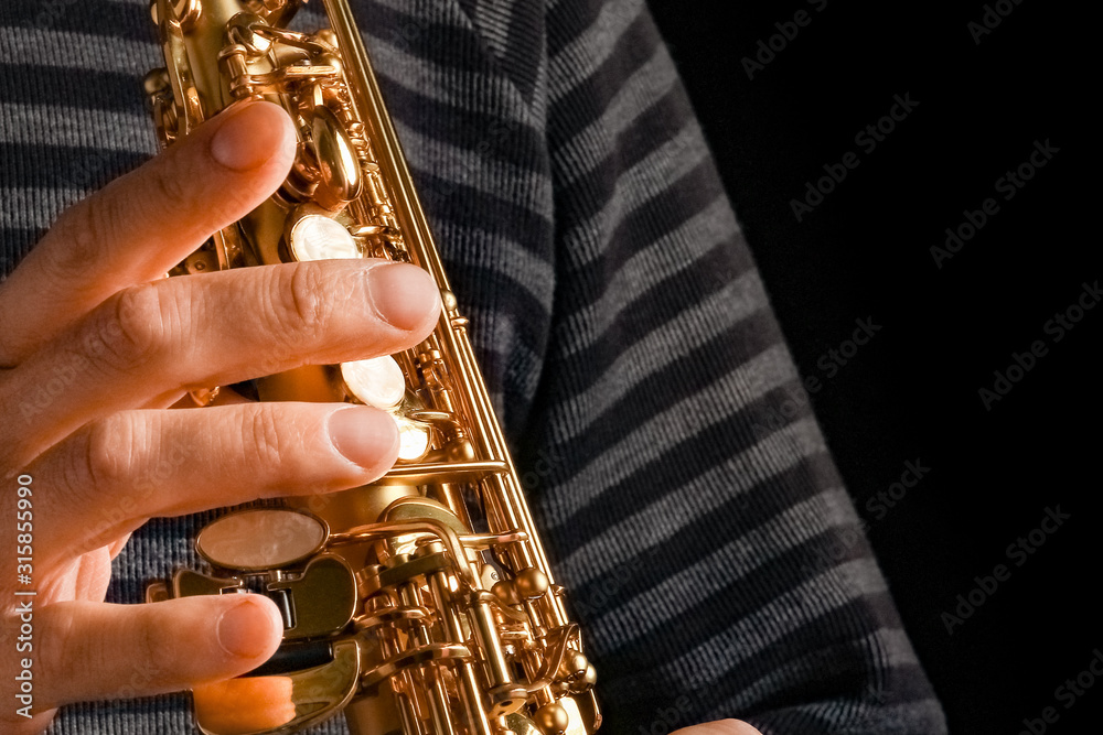 Obraz premium soprano saxophone in the hands of a guy on a black background