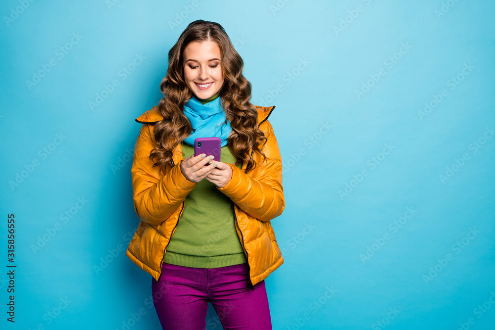 Photo of pretty millennial lady hold telephone hands searching best trip way information wear yellow overcoat scarf violet trousers green jumper isolated blue color background