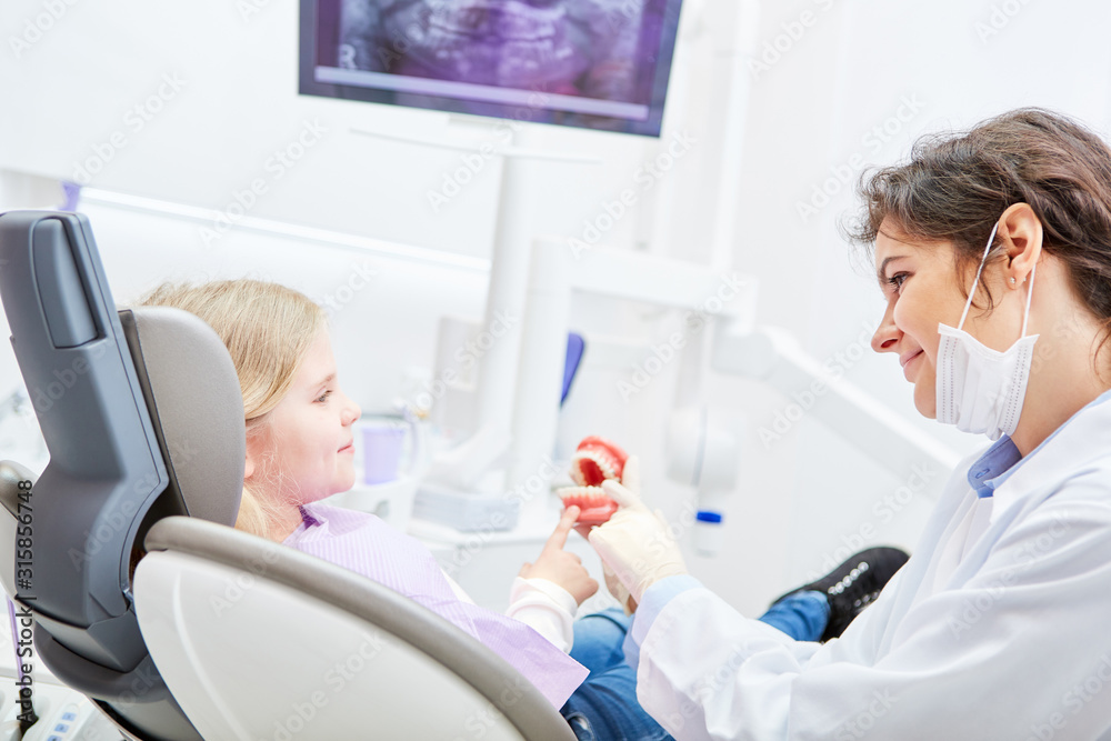 Dentist shows child as a patient a denture model Dentist shows child as a patient a denture model