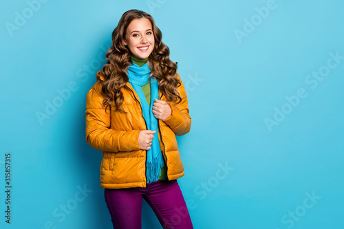 Photo of pretty curly lady toothy smiling amazing winter day walking street wear casual yellow overcoat blue scarf violet trousers isolated blue color background