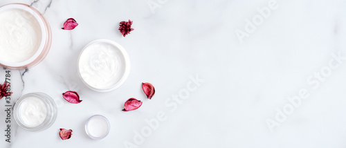 Banner mockup with cosmetic cream jars and pink petals on marble background. Natural organic beauty product concept. Top view, flat lay