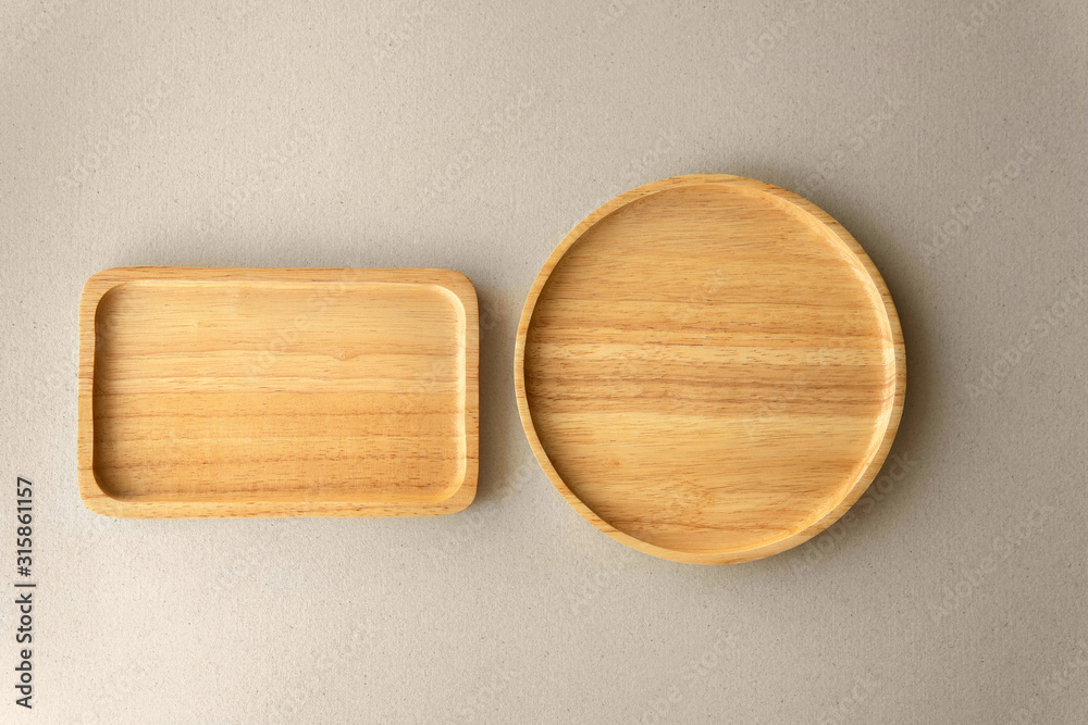 Top view empty above round wooden plate next to square tray on grey organic paper background. Top view empty above round wooden plate next to square tray on grey organic paper background.