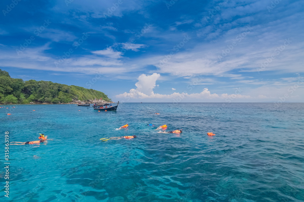 view of many tourists snorkeling in blue-green sea with cloudy sky background,  Tachai island, Mu Ko Similan National Park, Phang Nga, south of Thailand.