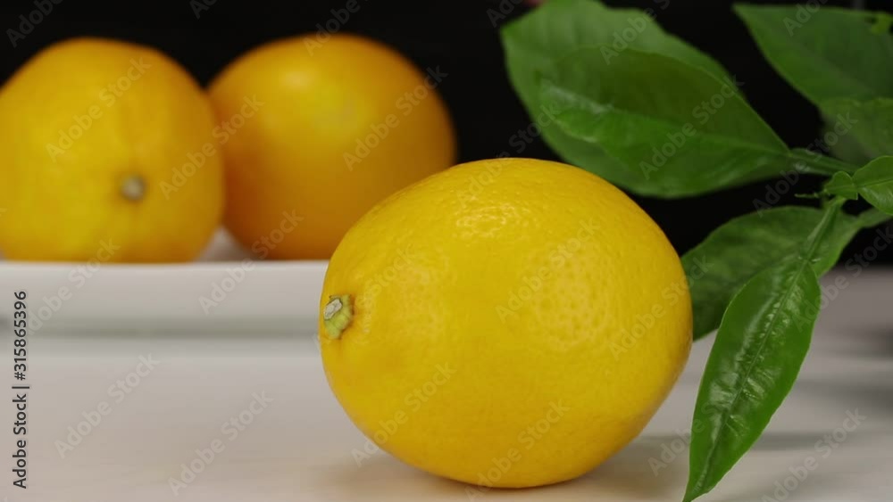 A large lemon lies in the foreground, in the background female hands put two lemons on a white plate A large lemon lies in the foreground, in the background female hands put two lemons on a white plate