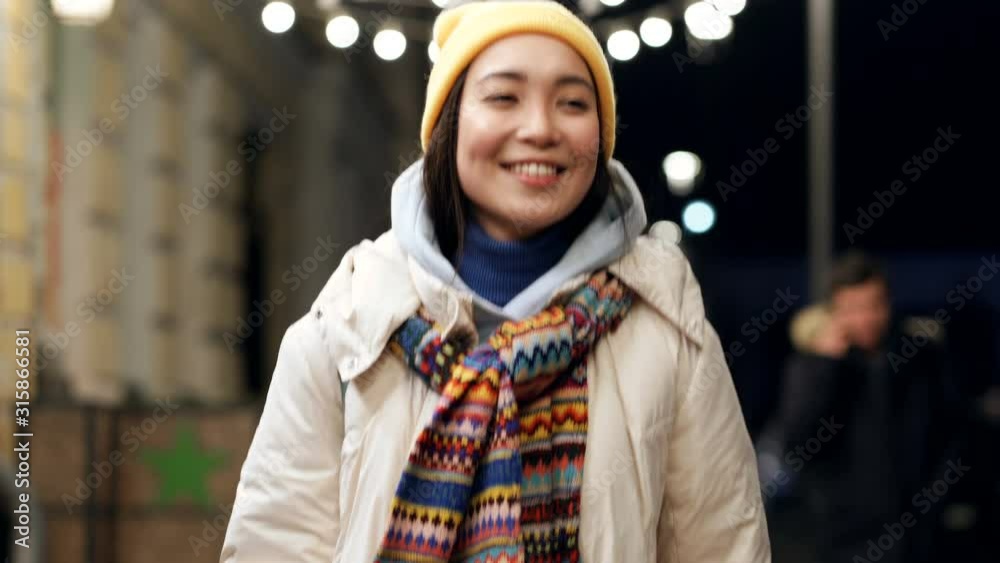 Smiling asian woman walking at the evening winter street. Gimbal shot.
