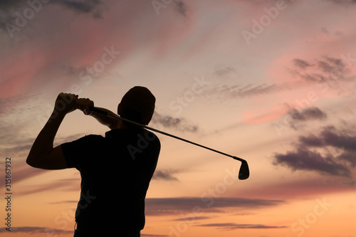 Golfer swinging a golf club silhouetted against a dusk sky photo