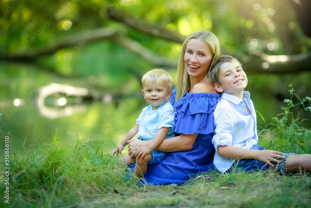 Children with the mother sitting on the lawn in the forest under a tree.