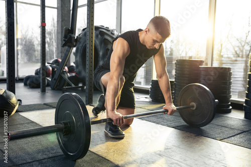 Overgoing. Young muscular caucasian athlete training in gym, doing strength exercises, practicing, work on his upper body with weights and barbell. Fitness, wellness, healthy lifestyle concept.
