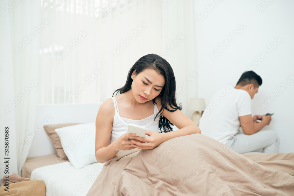 sad view of young married couple using their mobile phone in bed ignoring each other as strangers in relationship and communication problems sad view of young married couple using their mobile phone in bed ignoring each other as strangers in relationship and communication problems