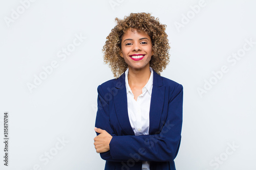 young woman african american looking like a happy, proud and satisfied achiever smiling with arms crossed against flat wall