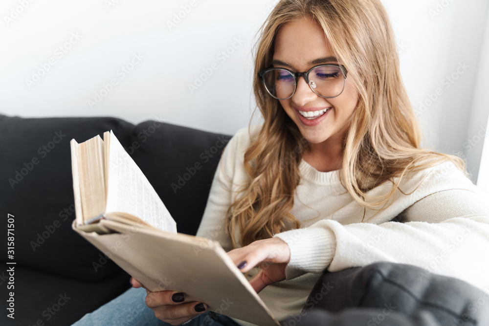 Photo of young smiling woman reading book while sitting on couch Photo of young smiling woman reading book while sitting on couch