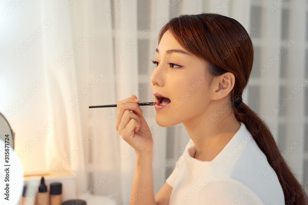 Portrait of young Asian woman applying lipstick with brush on lips Portrait of young Asian woman applying lipstick with brush on lips