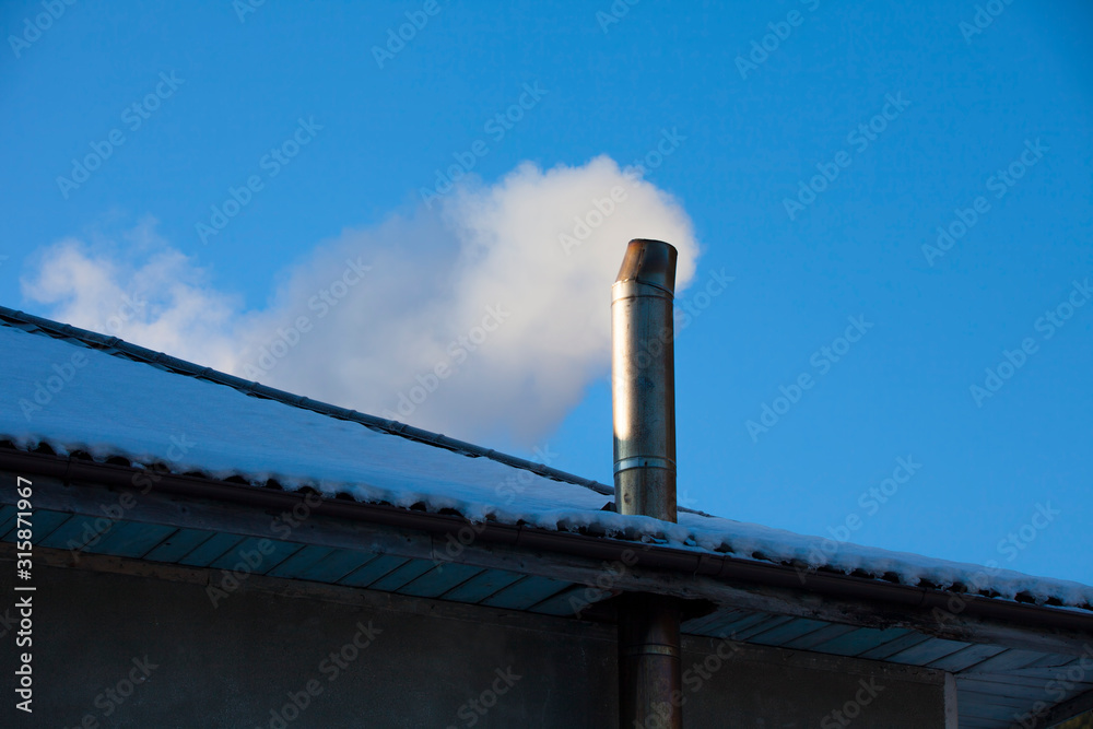 house chimney with smoke in winter scene. clear blue sky in the background house chimney with smoke in winter scene. clear blue sky in the background