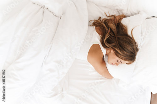 Photo of young caucasian woman sleeping and hugging pillow