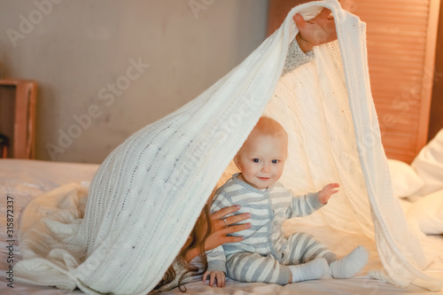 Baby and mom play on the white bed and hide under the covers.