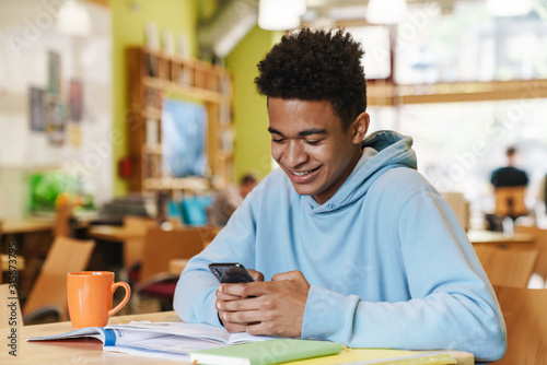Bild auf Leinwand Smiling african bot teenager studying while sitting at the hub