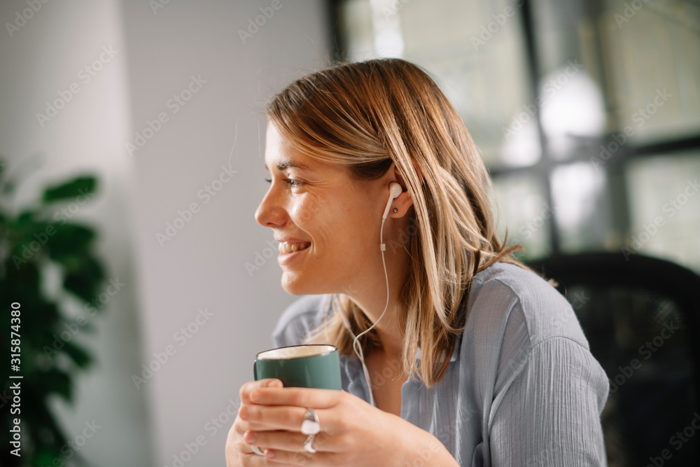 Young architect working on project in office. Beautiful businesswoman drinking coffee and listening music Young architect working on project in office. Beautiful businesswoman drinking coffee and listening music