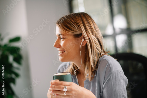 Young architect working on project in office. Beautiful businesswoman drinking coffee and listening music