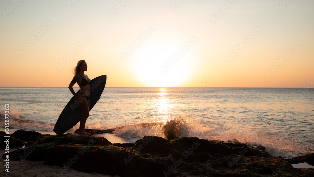 Surfing lifestyle. Surfer girl holding surfboard on the beach. Silhouette of surfer girl during sunset. Golden sunset time. Bali, Indonesia
