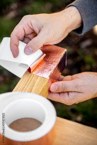 Man is affixing a copper tape on wooden beam, barrier and protection a raised bed photo