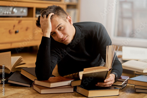 Young handsome student learns on the floor with books for exam 
