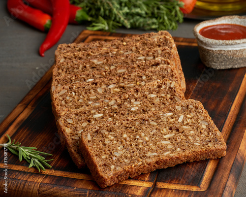 Toasted rye grain bread on a wooden cutting board on dark brown background. photo