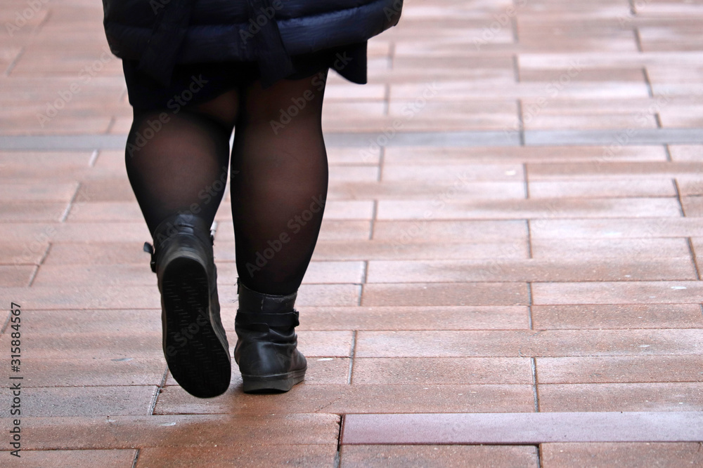 Fat woman walking down the street, thick legs in tights and black boots.  Concept of overweight and diet Stock Photo | Adobe Stock
