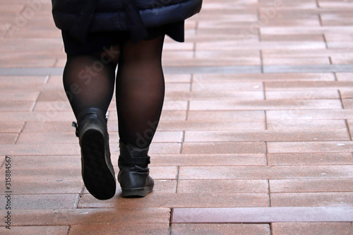 Fat woman walking down the street, thick legs in tights and black boots. Concept of overweight and diet