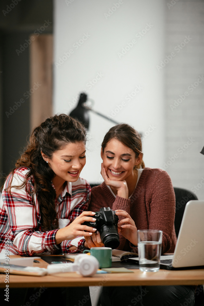 Young woman showing colleague pictures in camera. Two beautiful businesswomen having fun in office. Young woman showing colleague pictures in camera. Two beautiful businesswomen having fun in office.