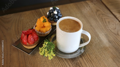 A cup of hot coffee with strawberry, mango, blueberry mini cupcakes on a wooden table.