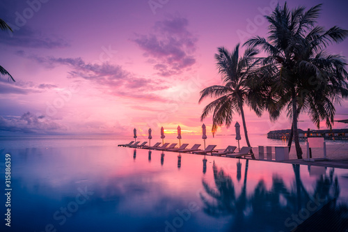 Beautiful poolside and sunset sky. Luxurious tropical beach landscape  deck chairs and loungers and water reflection.