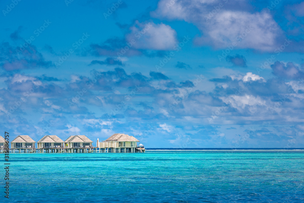 Luxury water villas in Maldives fantastic blue sea. Seascape and endless horizon under blue sky with clouds. Tropical nature pattern