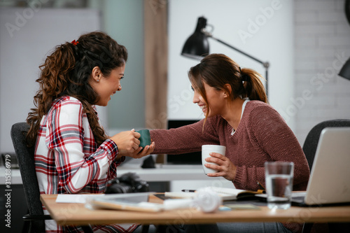 Two businesswomen having fun in office. Beautiful colleagues drinking coffee at work.
