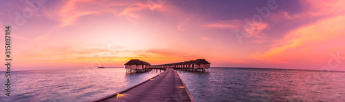 Sunset on Maldives island  luxury water villas resort and wooden pier. Beautiful sky and clouds and beach background for summer vacation holiday and travel concept