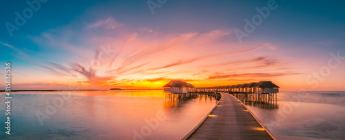 Sunset on Maldives island, luxury water villas resort and wooden pier. Beautiful sky and clouds and beach background for summer vacation holiday and travel concept