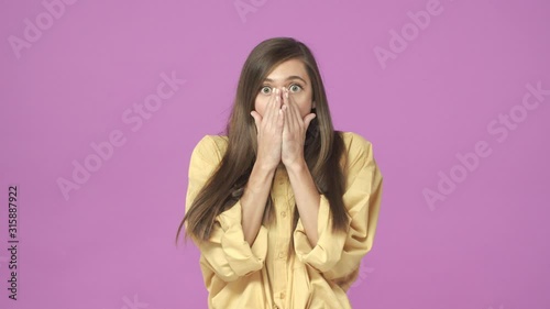 Slow-motion shook, astounded young speechless girl 20s, wearing shirt, reacting surprised and startled at something unexpected and shocking, standing purple background gasping, cover mouth