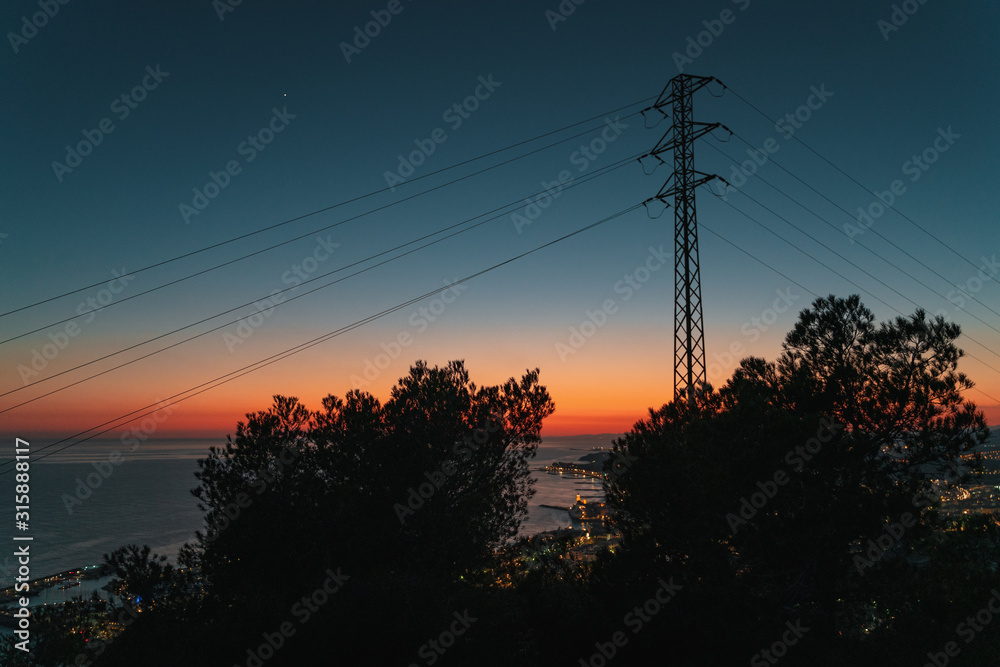 Low angle view of electricity pylon against illuminated city by night