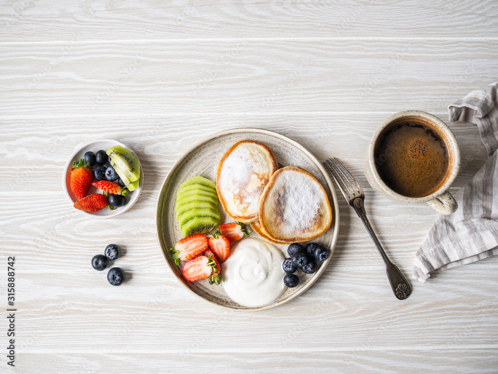 Delicious breakfast - fritters pancakes, sprinkled with powdered sugar with fruits and berries and sour cream Delicious breakfast - fritters pancakes, sprinkled with powdered sugar with fruits and berries and sour cream