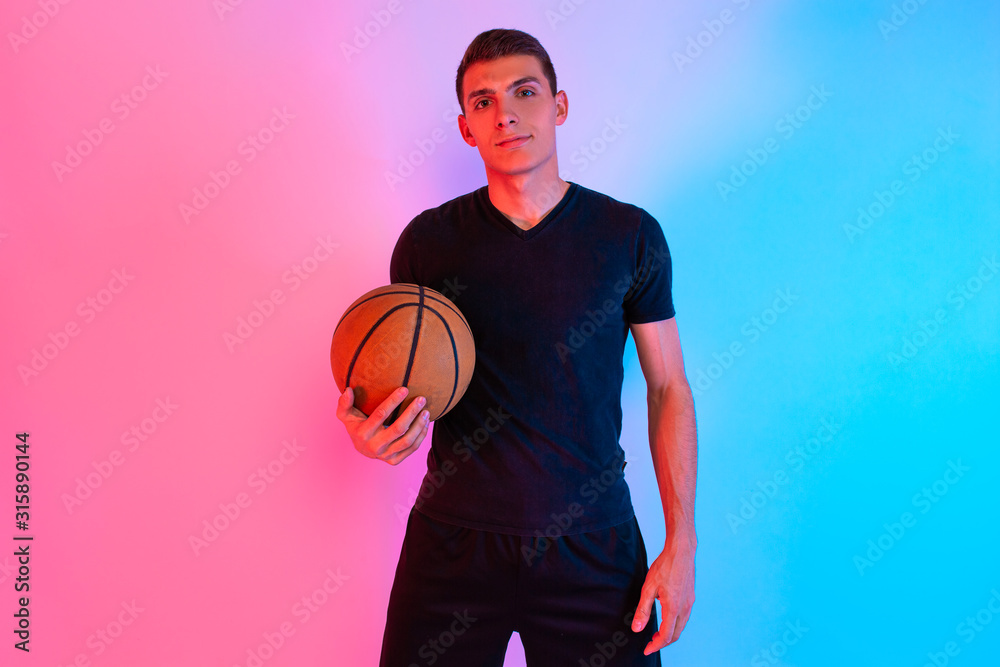 Naklejka premium Young athletic man, with basketball, posing on background with neon lights