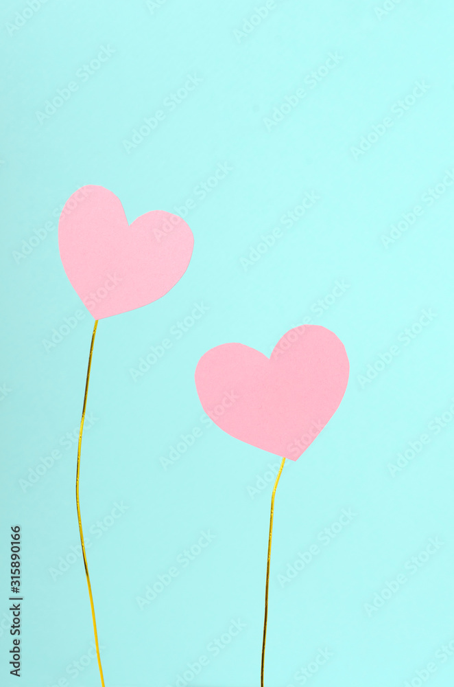 Two sweet pink paper hearts on the colored gold wire against blue background. Concept of couple in love